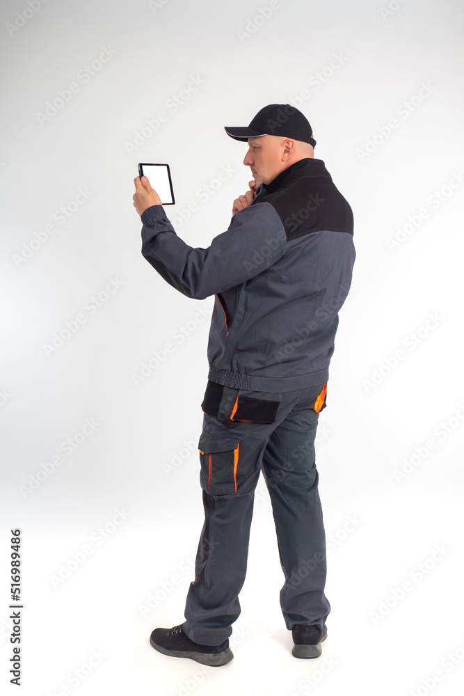 Wall mural portrait of a worker with a tablet in his hands. a man in a gray uniform stands sideways and looks a