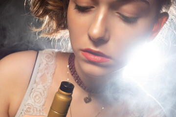 The girl smokes VAPE. The girl looks at the electronic cigarette. A woman with a VAPE in a cloud of...