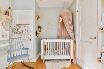 Interior of white room with baby crib and armchair near window with blue chest of drawers in daylight - obrazy, fototapety, plakaty