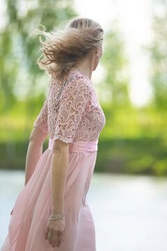A beautiful woman in a flowing pink dress stands on her back to the camera.
