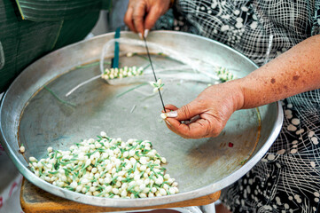 A street seller is making  a JAsmin necklace in Thailans