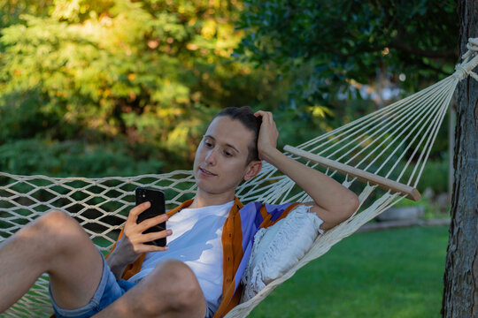 Portrait of young hipster man resting in a hammock looking to his smartphone as leisure activity in free time