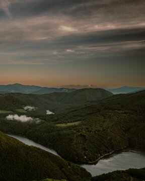 Vertical shot of huge greenery mountains surrounded by water during susnet