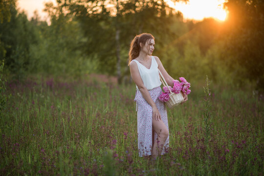 Beautiful happy young girl with peonies in nature outdoors in the sun. Beautiful woman in a field with flowers in a long skirt