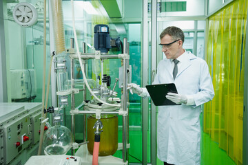 Caucasian male scientist with lab coat, gloves and glasses is monitoring pressure and temperature...