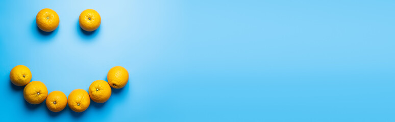 Top view of ripe oranges in smile shape on blue background, banner.