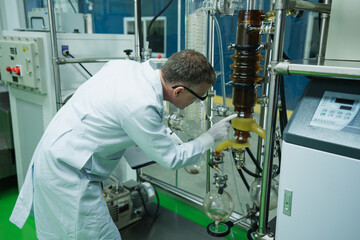 In marijuana laboratory, Caucasian researcher in lab uniform is pointing to rotational vaporizer...