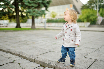 Funny toddler boy having fun outdoors on sunny autumn day. Child exploring nature. Kid walking in a city park.