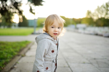 Funny toddler boy having fun outdoors on sunny autumn day. Child exploring nature. Kid walking in a city park.