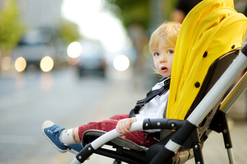 Naklejka premium Sweet toddler boy sitting in a stroller outdoors. Little child in pram. Infant kid in pushchair. Summer walks with kids.