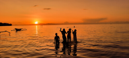 Silhouette of four children playing on the beach with sunset background and boats. Sunset on the beach. Silhouette of childrens. Sunset Beach Vacation Outdoor Summer holiday Background.