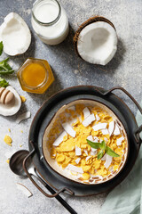 Vegan healthy breakfast. Cereal granola breakfast flakes with coconut non-dairy alternative milk and fresh coconut slices on a stone tabletop. View from above.
