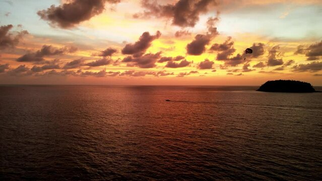 Aerial View Of Parasailer Being Pulled By Boat Against Golden Orange Sunset Skies Over Tropical Waters Off Phuket. Dolly Forward
