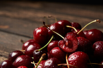 Close up of pile of sweet red cherries with stalks and leaves on a wooden table. Black background. Food and fruit concept. Space for your text
