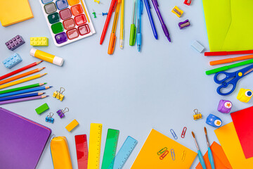 The concept of back to school. Colorful school supplies lie in the form of a frame on a gray-blue background. Books, notebooks, pens, paper clips, paints and markers.
