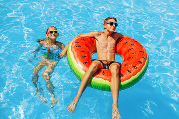 boy and a girl swim in the outdoor pool. Summer holidays with children. Swimming aids and children's clothing