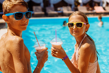 Child with drink in the outdoor pool. Children swim in a tropical resort. Healthy exotic fruit refreshing drink for kids