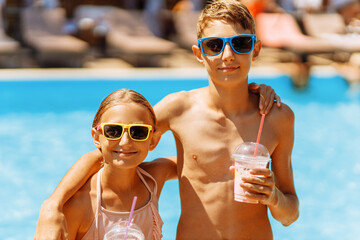 Two happy children, a girl and a boy, drink juice in the pool and have fun