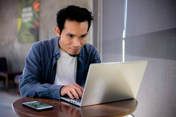 Fototapeta premium Asian man sitting and using laptop at coffee shop
