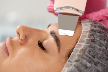 Cosmetologist, beautician in pink gloves making facial treatment with ultrasonic spatula to woman,...