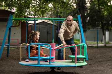 divorced father walks with his little daughter, he rolls her on a round swing in the courtyard of...