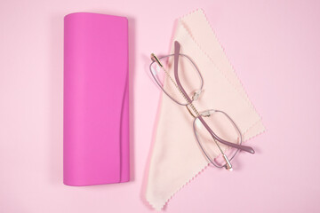 Obraz na płótnie Canvas Pink frame womens glasses with glasses cleaning cloth and case on a pink background.