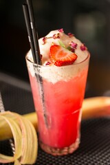 Vertical shot of a pink cocktail with cream and strawberry topping - Italian soda