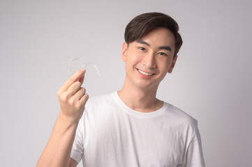 Young smiling man holding invisalign braces over white background studio, dental healthcare and Orthodontic concept..