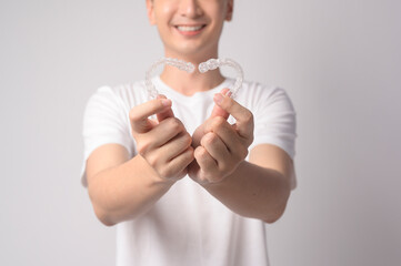 Young smiling man holding invisalign braces over white background studio, dental healthcare and Orthodontic concept.. - obrazy, fototapety, plakaty