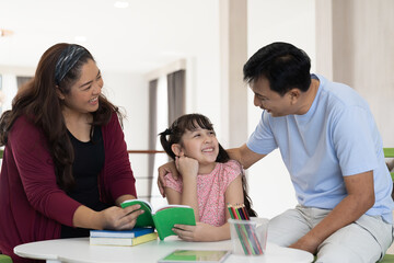 Obraz premium Diverse asian family with child daughter reading a book together at home. Smiling parents and teen daughter spending time together.