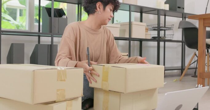 Asian Attractive Woman Working From Laptop Verifying E-commerce Post Shipping Online Retail E-commerce Shop Order Fulfillment At Drop Shipping Delivery Warehouse While Preparing Parcel Boxes.