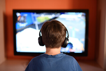 Child with headphones on his back in front of the TV