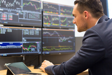Stock broker trading online while accepting orders by phone. Trader's office with multiple computer screens full of index charts and data analyses