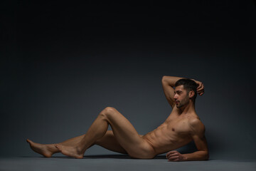 Fashion nude photo of a male model with seductive figure lying isolated on the floor in a studio