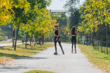 Obraz premium Full body portrait of happy sportswomen rollerskating in the park on a sunny day