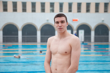 Obraz premium Portrait of a fit swimmer man at pool looking at camera. Portrait of competitive male swimmer near swimming pool.