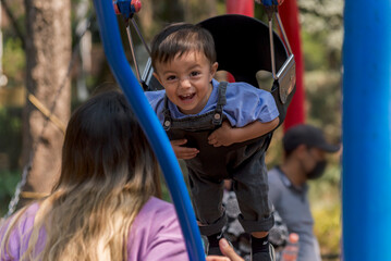 Young baby boy playing with his mom on the swing at the park