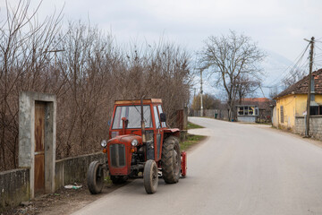 Old abandoned agriculture orange Tractor parked on countryside street.