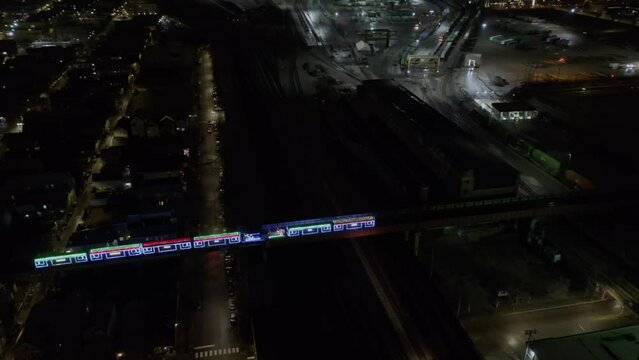 Aerial drone shot over a metro train lit up with colorful neon lights in Chicago at night time in USA. 