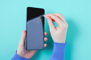 Removes a transparent protective film from new smartphone. Turquoise background.