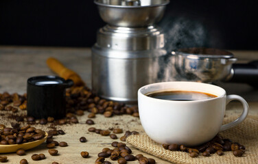 Cup of black Americano coffee on a wooden table with a pile of roasted Arabica coffee beans on black background.