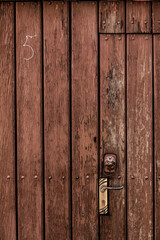 wooden door made of longitudinal boards with a handle and the number 5 drawn in chalk as a vertical background