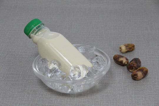 A bottle of Dates Milk served in iced cube bowl side view on grey background