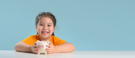 Asian cute girl saving money putting coins into piggy bank on table at home, learning about saving, Kid save money for future education. Money, finances, insurance, and people concept