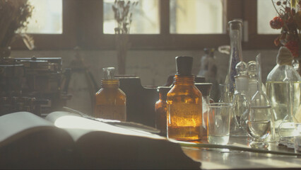Close-up of a perfumer's workplace. Vintage cinematic concept. Sunny day in the working workshop. Lots of ingredients, a book, glass flasks on the table. Depth of field