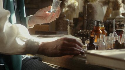 A close-up of a perfumer at his desk looking for a new fragrance. Vintage cinematic concept. Sunny day in the workshop. Lots of ingredients, glass flasks on the table. Concept of perfumery