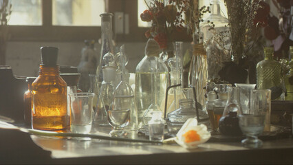 Close-up of a perfumer's workplace. Vintage cinematic concept. Sunny day in the working workshop. Lots of ingredients, a book, glass flasks on the table. Depth of field - obrazy, fototapety, plakaty