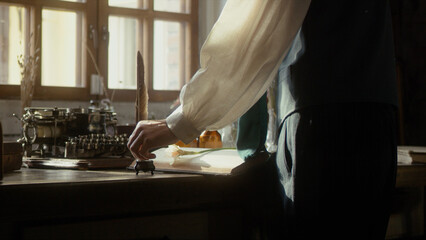 A man writer dips his pen into an inkwell and prepares to write a book in his workshop. Cosplay of...