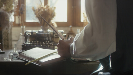 A man writer dips his pen into an inkwell and prepares to write a book in his workshop. Cosplay of the Middle Ages. Cinematic concept. Close-up feather
