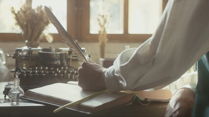 A man writer dips his pen into an inkwell and prepares to write a book in his workshop. Cosplay of the Middle Ages. Cinematic concept. Close-up feather